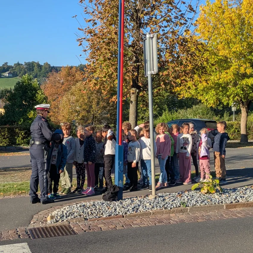 Ein Polizist gibt einer Gruppe von Kindern am Straßenrand eine Sicherheitseinweisung.