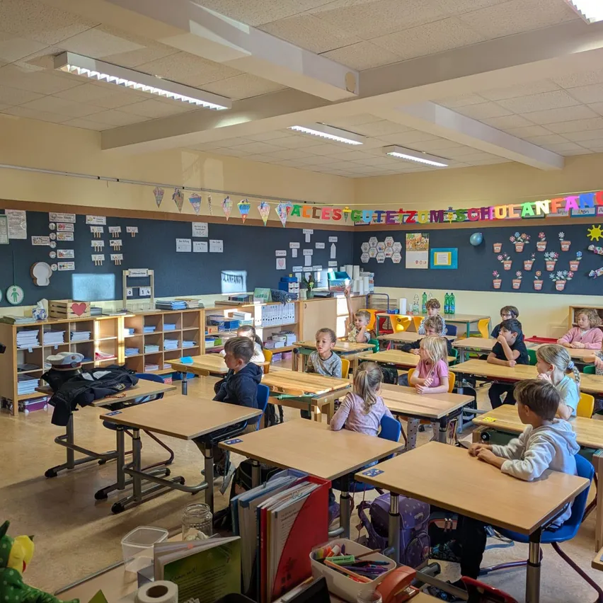 Ein Klassenzimmer mit Schülern an Schreibtischen, ein Polizist steht in der Nähe der Tür.
