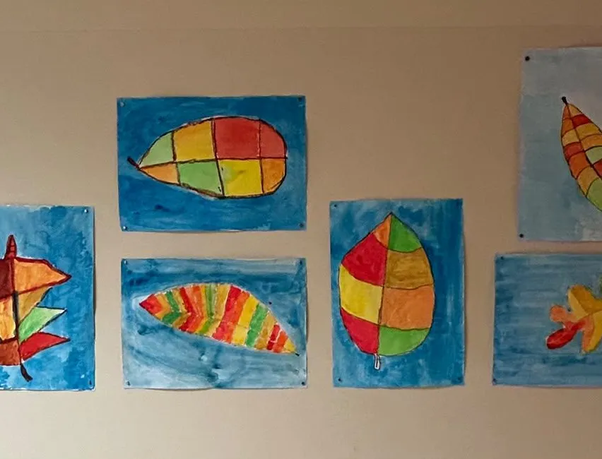 Eine Reihe bunter Blattgemälde an einer Wand. Jedes Blatt ist in einer anderen Stil- und Farbkombination gemalt.