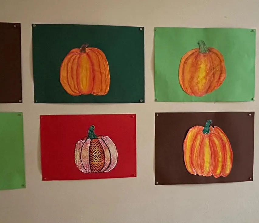 Eine Sammlung von neun Kürbisgemälden, jedes auf einem anderen farbigen Hintergrund, ist an einer weißen Wand ausgestellt.