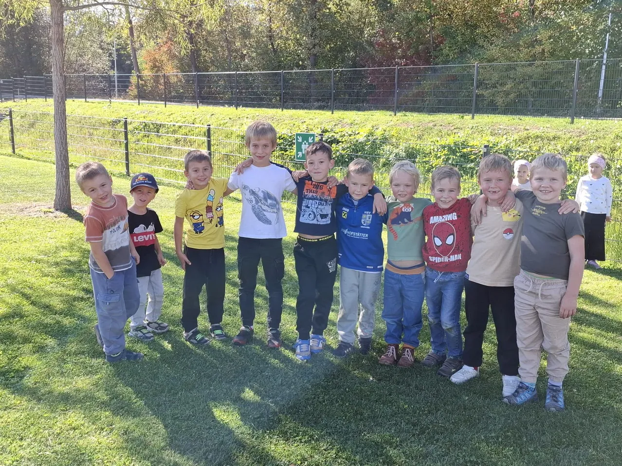 Eine Gruppe junger Jungen steht zusammen auf einem Rasenfeld. Sie alle lächeln und scheinen für ein Foto zu posieren.