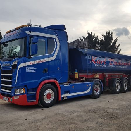 Ein blauer LKW mit weißen Zierleisten steht auf einer unbefestigten Straße. Er hat den Text Karl Duskamich an der Seite.