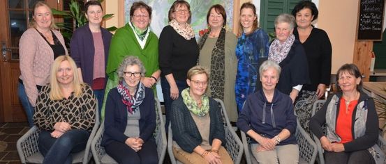 Eine Gruppe von Frauen, einige sitzend und einige stehend, posiert für ein Foto in einem Raum mit einem Gemälde an der Wand.