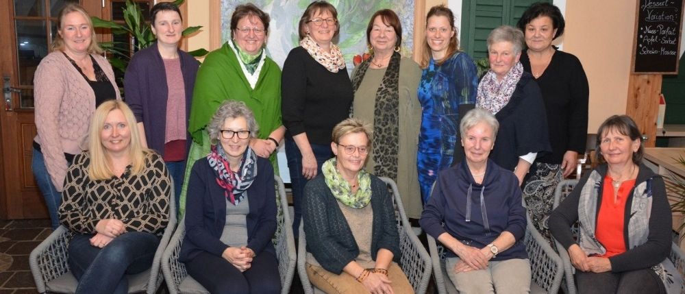 Eine Gruppe von Frauen, einige sitzend und einige stehend, posiert für ein Foto in einem Raum mit einem Gemälde an der Wand.