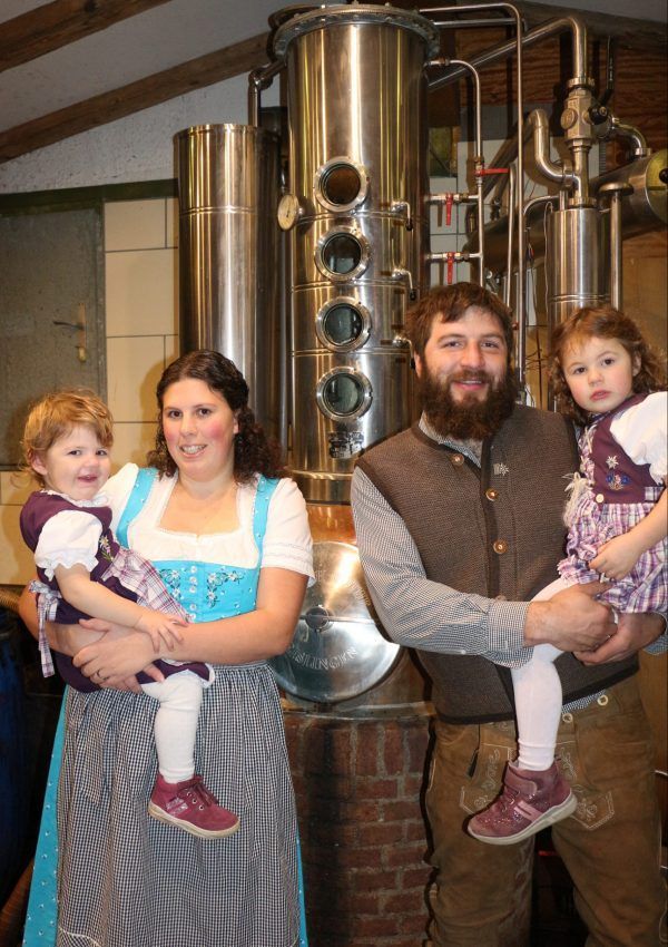 Eine Familie mit vier Personen steht vor großen silbernen Tanks in einem Fabrikambiente. Ein Mann und eine Frau halten jeweils ein Kind.
