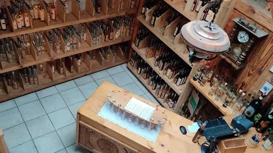 Ein Laden mit Holzregalen gefüllt mit verschiedenen Flaschen und Gläsern, einer hölzernen Theke mit Laptop, Maus und Korb und einer von der Decke hängenden Lampe.
