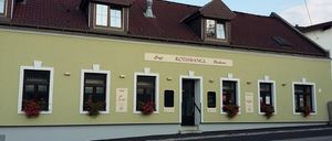 Ein gelbes Gebäude mit braunem Dach, weißer Einfassung und roten Blumen in Kisten. Es trägt den Namen Rothwangl Bäckerei über dem Eingang.