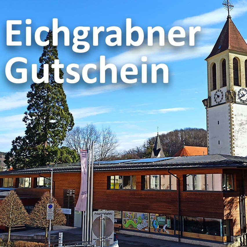 Ein Foto eines Gebäudes mit einem Turm und Solarmodulen auf dem Dach, mit dem Text 'Chgrabner Utschchein' in weißer Schrift. Bäume umgeben das Gebäude. Eine Uhr befindet sich auf dem Turm.