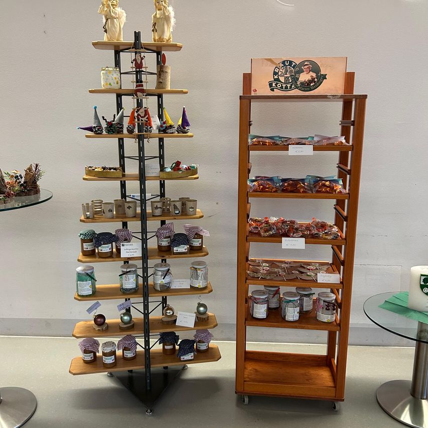 Two wooden shelves display various products. One shelf has jars of honey and small ornaments, while the other has boxes of candies. Both shelves have a white label on the middle shelf.