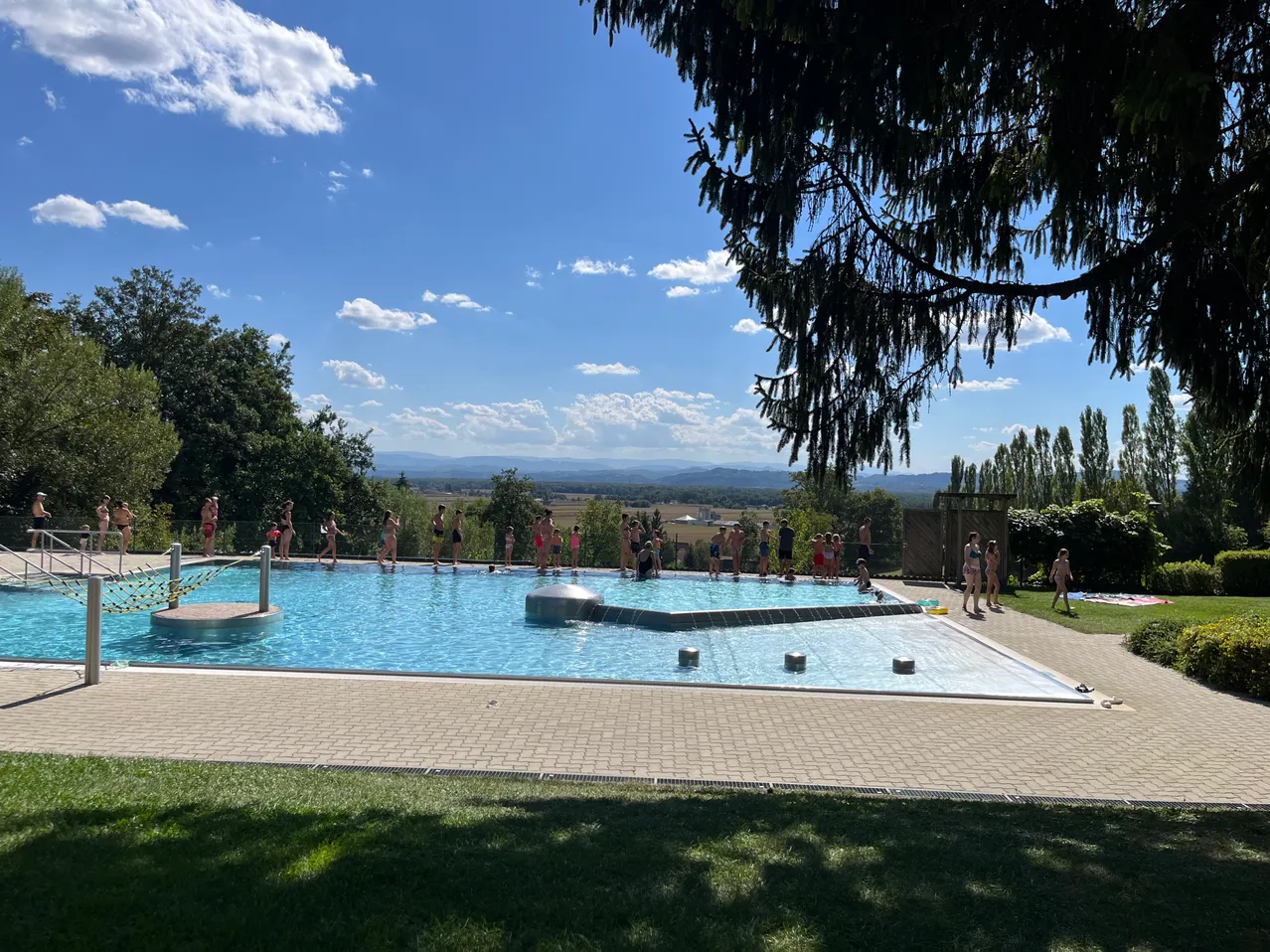 Ein großer Außenpool mit Menschen, die schwimmen und an einem sonnigen Tag herumstehen.