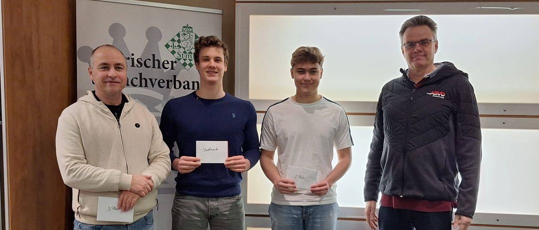 Vier Männer stehen zusammen und halten Urkunden in der Hand. Sie befinden sich in einem Raum mit einem weißen Banner hinter ihnen. Sie lächeln und schauen nach vorne.