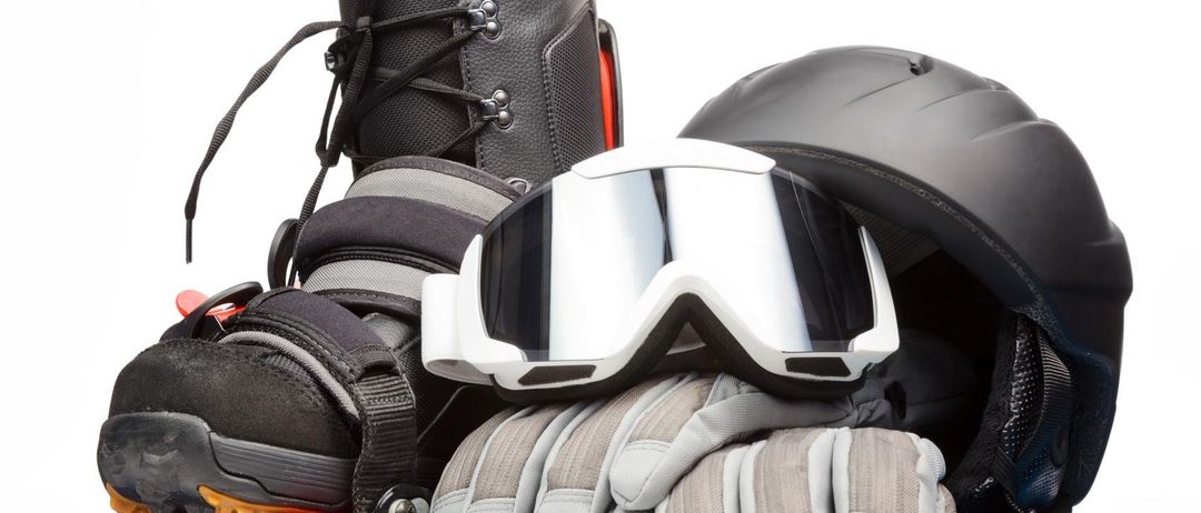 Ein Set aus schwarzen Skischuhen, eine Brille, ein Helm und Handschuhe liegen auf einem blauen Snowboard.