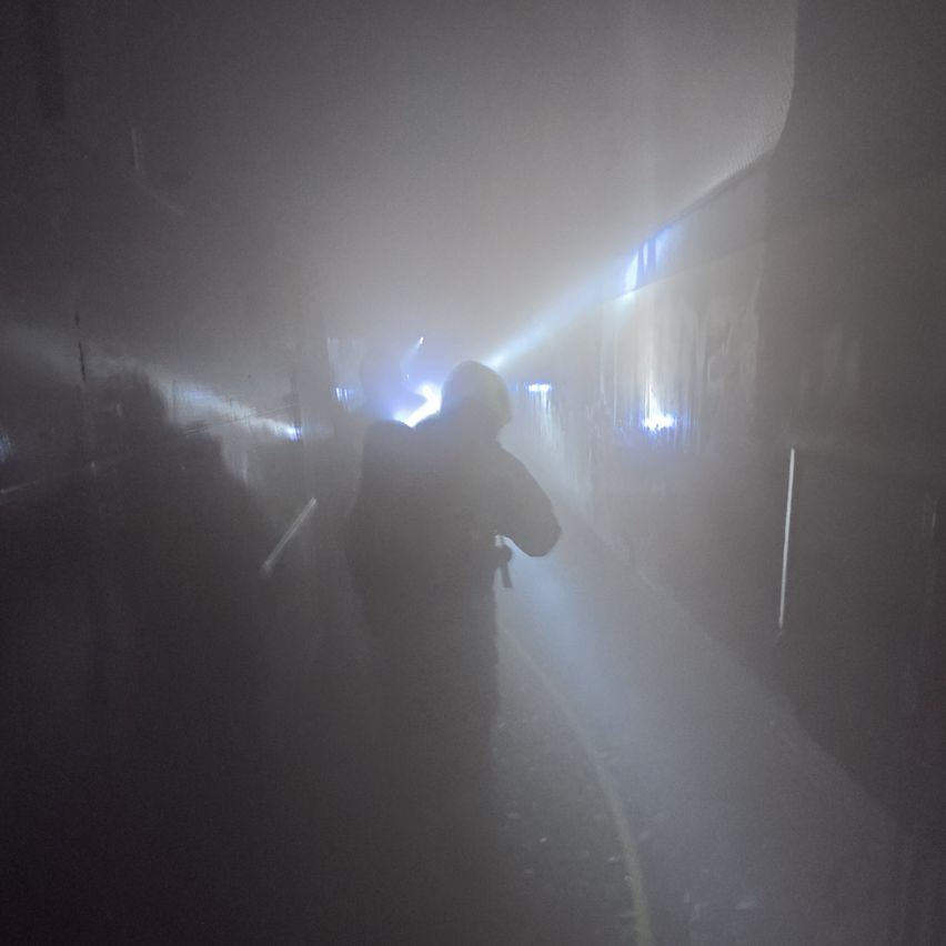 Ein Feuerwehrmann steht in einem schwach beleuchteten, nebligen Tunnel mit einer Taschenlampe. Die Wände sind von blauen Lichtern beleuchtet.