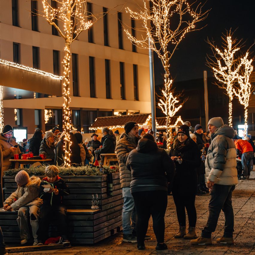 Bei Nacht versammelt sich eine Gruppe von Menschen unter festlich beleuchteten Bäumen und genießt die Atmosphäre eines Wintermarktes.