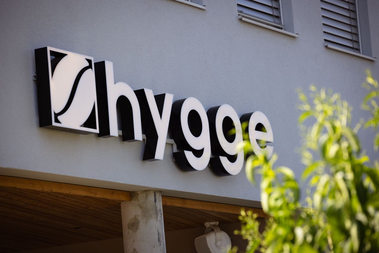 Ein weißes und schwarzes Schild für 'hygge' an einer grauen Wand mit einem Fenster darüber.