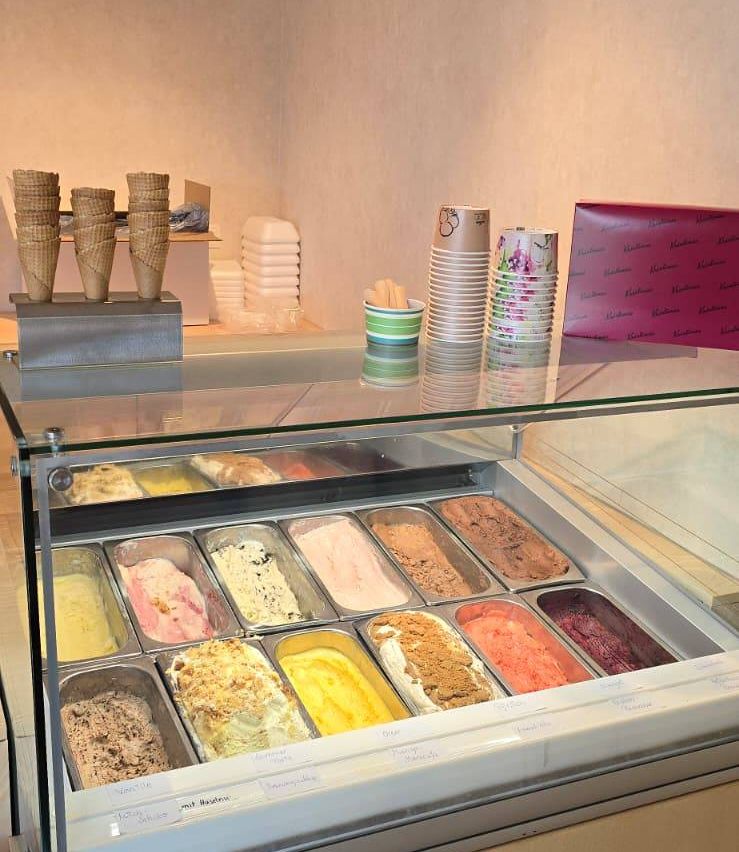 Eine Glasvitrine mit verschiedenen Eissorten, mit Eisbechern und Tassen im Hintergrund.