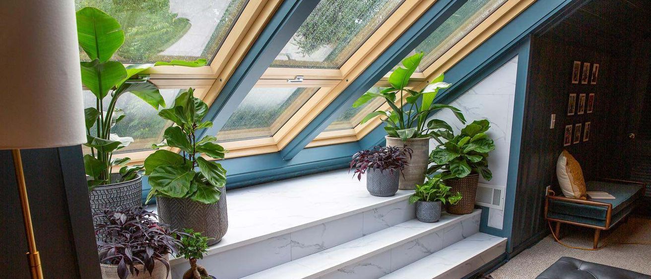 Eine Marmortreppe mit mehreren Topfpflanzen unter einem Dachfenster. Der Raum hat Holzböden und eine Lederbank.