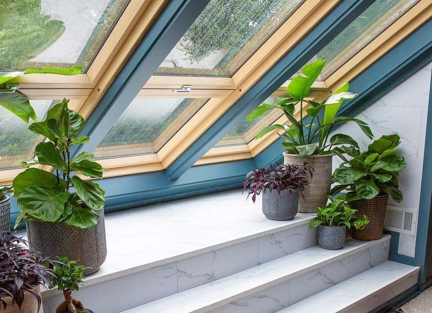 Eine Marmortreppe mit mehreren Topfpflanzen unter einem Dachfenster. Der Raum hat Holzböden und eine Lederbank.