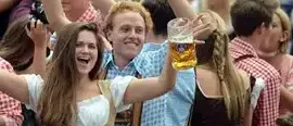 Eine Gruppe von Menschen auf einem Festival, einige heben ihre Hände und halten Biergläser hoch, während andere traditionelle Kleidung und Hüte tragen.