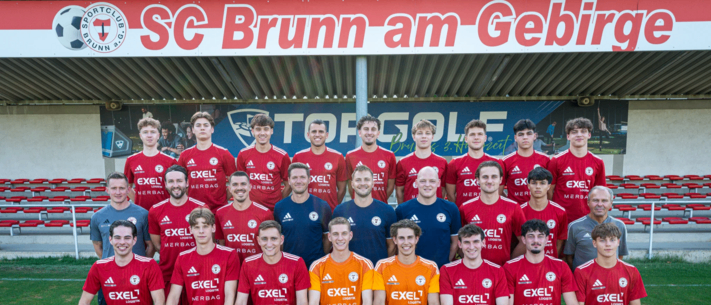 Eine Fußballmannschaft posiert für ein Gruppenfoto auf einem Feld mit einem Banner im Hintergrund, das SC Brunn am Gebirge liest.