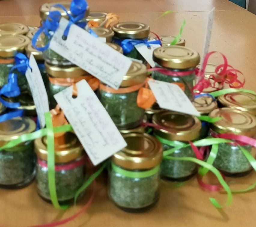 Eine Sammlung von kleinen Gläsern mit grünem Inhalt, jedes mit einem Etikett und einer Schleife, auf einer Holzoberfläche angeordnet.