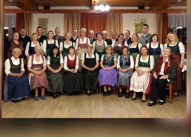 Eine Gruppe von Menschen in traditioneller Kleidung posiert für ein Foto in einem Raum mit Holzboden und Vorhängen.