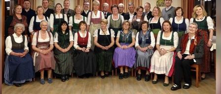 Eine Gruppe von Menschen in traditioneller Kleidung posiert für ein Foto in einem Raum mit Holzboden und Vorhängen.