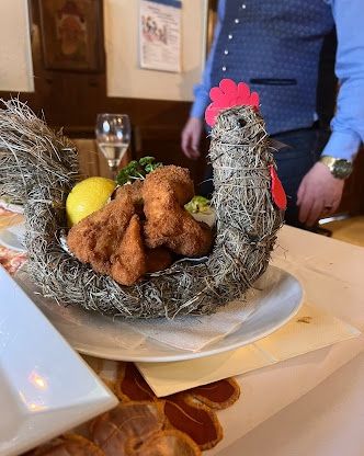Ein Gericht in Form eines Huhns in einem Zweigkorb mit frittierter Nahrung und einer Zitrone steht auf einem Tisch mit Tischdecke. Eine Person steht dahinter.