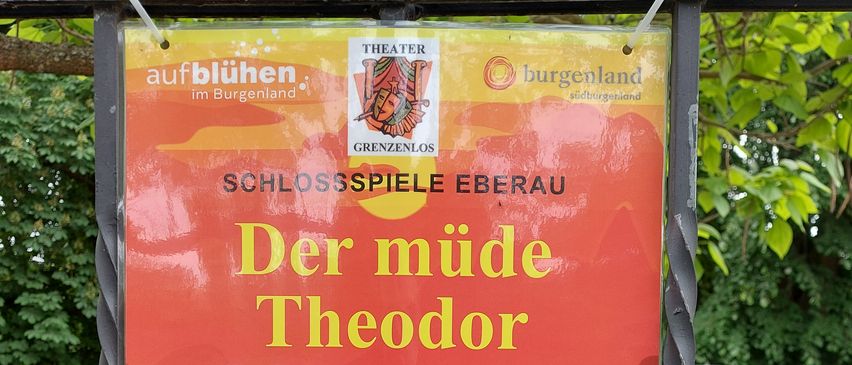 Ein rotes Plakat bewirbt 'Der müde Theodor' in drei Akten. Die Termine sind 13., 14., 15., 20., 21., 22. Juni 2025. Zeiten sind 20:00 Uhr Freitags und Samstags, und 18:30 Uhr Sonntags. Kontakt 0681/10 30 9200.