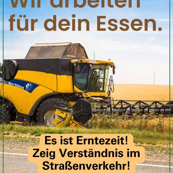 Ein gelber New Holland Mähdrescher erntet auf einem sonnigen Tag Getreide. Eine Person fährt den Mähdrescher. Der Bildtext lautet 'Wir arbeiten für dein Essen. Es ist Erntezeit! Zeige Verständnis im Straßenverkehr!'