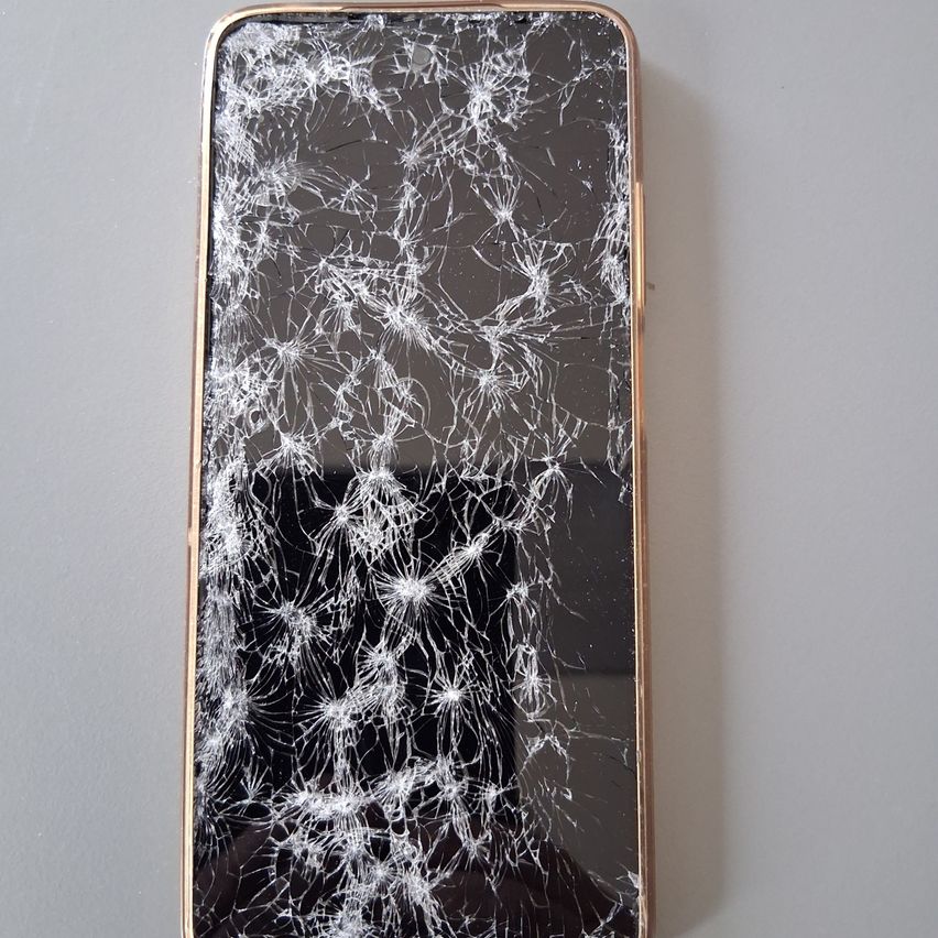 Ein Smartphone mit einem gebrochenen Bildschirm und einem goldenen Rand, vor einem grauen Hintergrund dargestellt.