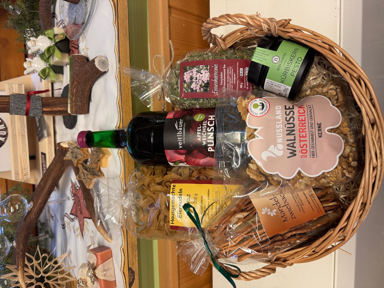 Ein Korb mit einer Flasche Sauce, Nüssen, einem Glas Pesto, einer Tüte Kräuter und einer Schachtel Pasta.