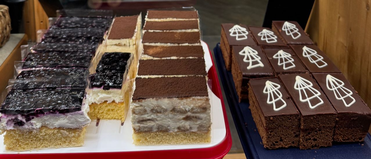 Ein roter Teller enthält mehrere Desserts, darunter ein mehrschichtiger Kuchen mit Schokolade und Sahne und ein Kuchen mit einem weißen Baumdesign auf der Oberseite.