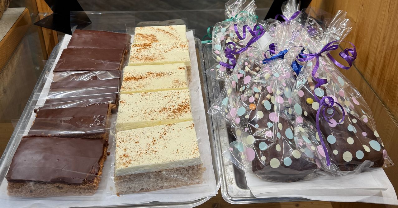 Zwei Tabletts mit Desserts sind ausgestellt. Eines hat Käsekuchenstücke mit Zimt bestreut. Das andere hat schokoladenüberzogene Leckereien in farbenfrohen Verpackungen.