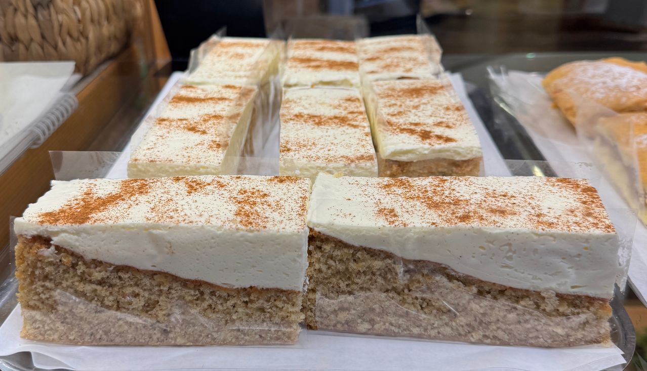 Mehrere Kuchenscheiben mit weißer Glasur und einer Zimtstreuung sind auf einer weißen Oberfläche angeordnet.