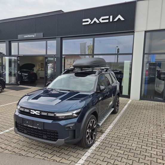 Ein blauer Dacia SUV mit Dachgepäckträger steht vor einem Dacia-Händler.