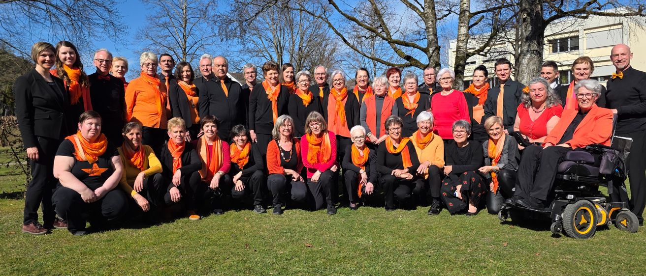 Eine Gruppe von Menschen mit orangefarbenen Schals posiert auf einem Rasen für ein Foto.