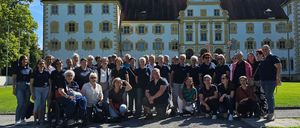 Eine große Gruppe von Menschen in ähnlicher Kleidung posiert für ein Foto vor einem historischen Gebäude mit gelben Fensterläden.