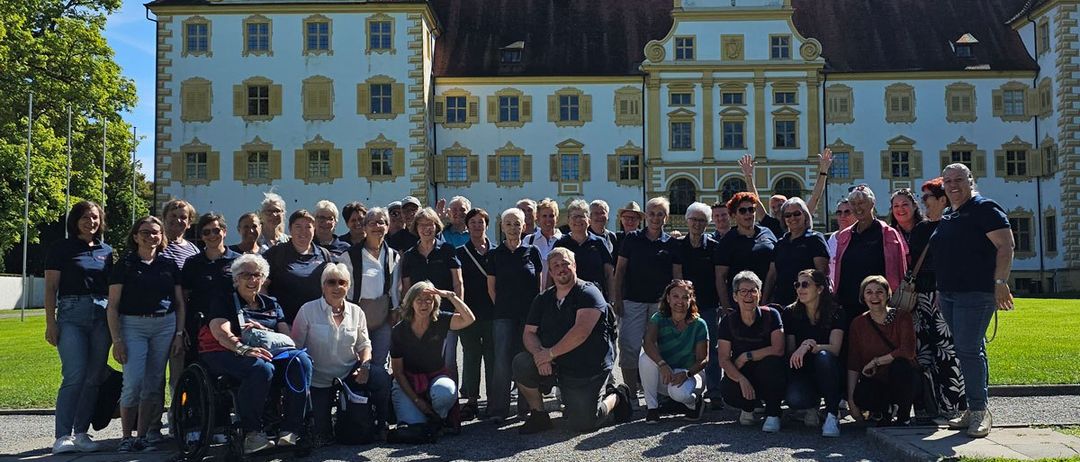 Eine große Gruppe von Menschen, darunter sowohl Männer als auch Frauen, posiert für ein Foto vor einem großen Gebäude mit vielen Fenstern.