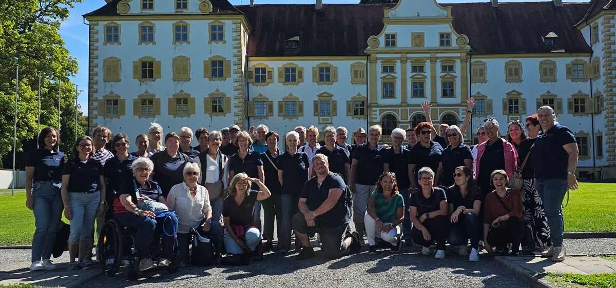 Eine große Gruppe von Menschen, darunter sowohl Männer als auch Frauen, posiert für ein Foto vor einem großen Gebäude mit vielen Fenstern.
