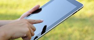 Eine Person hält ein Tablet in den Händen und berührt den Bildschirm mit dem Daumen, möglicherweise im Freien.