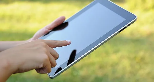 Eine Person hält ein Tablet in den Händen und berührt den Bildschirm mit dem Daumen, möglicherweise im Freien.