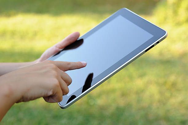 Eine Person hält ein Tablet in den Händen und berührt den Bildschirm mit dem Daumen, möglicherweise im Freien.