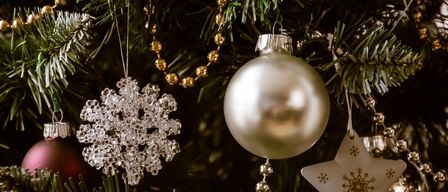 Ein Nahaufnahme eines Weihnachtsbaums, geschmückt mit Ornamenten. Eine große silberne Kugel ist zentral positioniert mit einem Kristall-Schneeflocken und einem goldenen Stern in der Nähe.