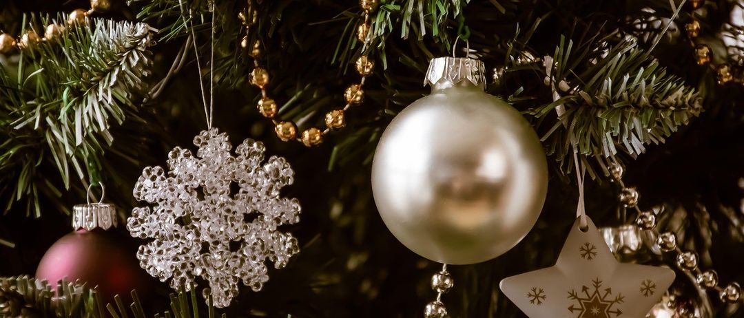 Ein Nahaufnahme eines Weihnachtsbaums, geschmückt mit Ornamenten. Eine große silberne Kugel ist zentral positioniert mit einem Kristall-Schneeflocken und einem goldenen Stern in der Nähe.
