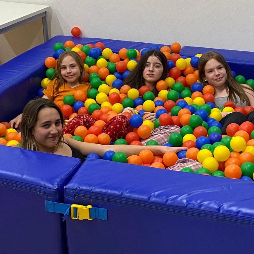 Vier Mädchen spielen in einem großen Ballpool voller bunter Bälle. Sie lächeln und scheinen sich zu amüsieren.