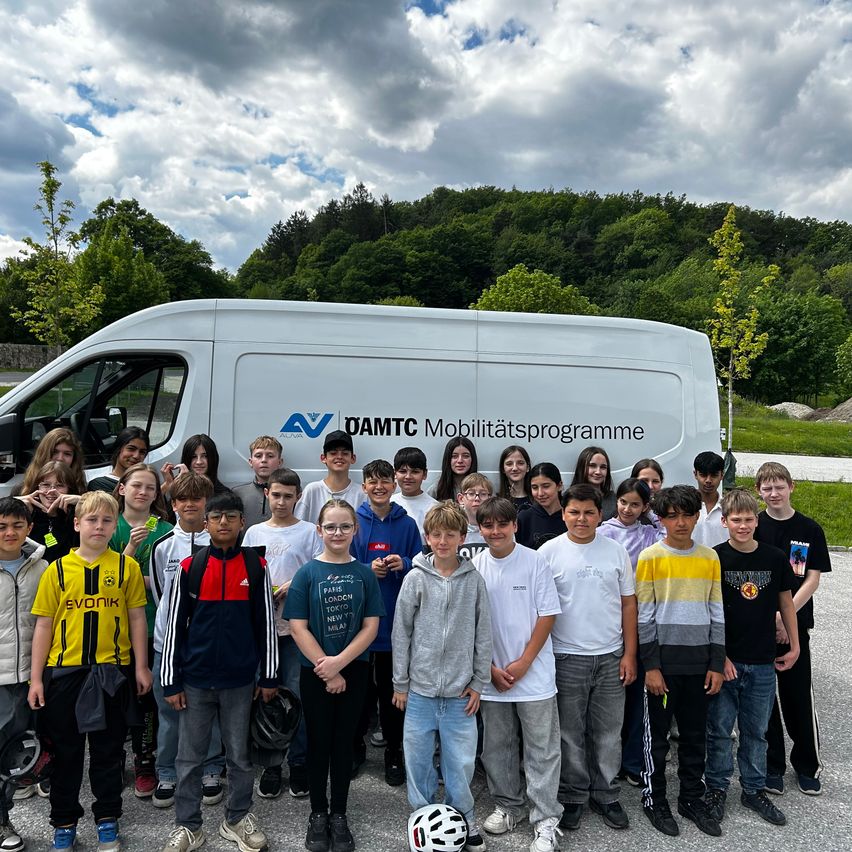 Eine Gruppe von Kindern und Jugendlichen steht vor einem weißen Van mit dem Logo des DAMTC Mobilitätsprogramms an einem bewölkten Tag.