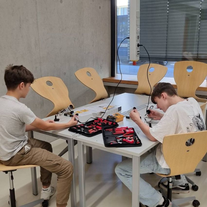 Schüler löten im Technikunterricht in einer Schule in Österreich an einem Tisch mit Werkzeug.