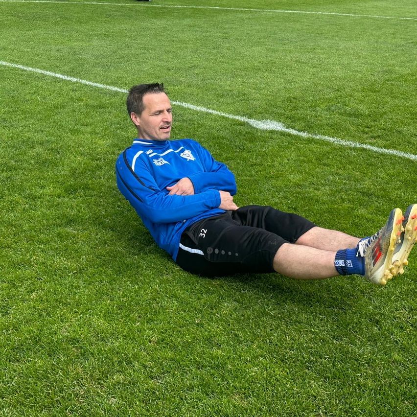 Ein Mann in Blau ruht sich auf dem Rasen eines Fußballfeldes aus, mit blauen Socken.