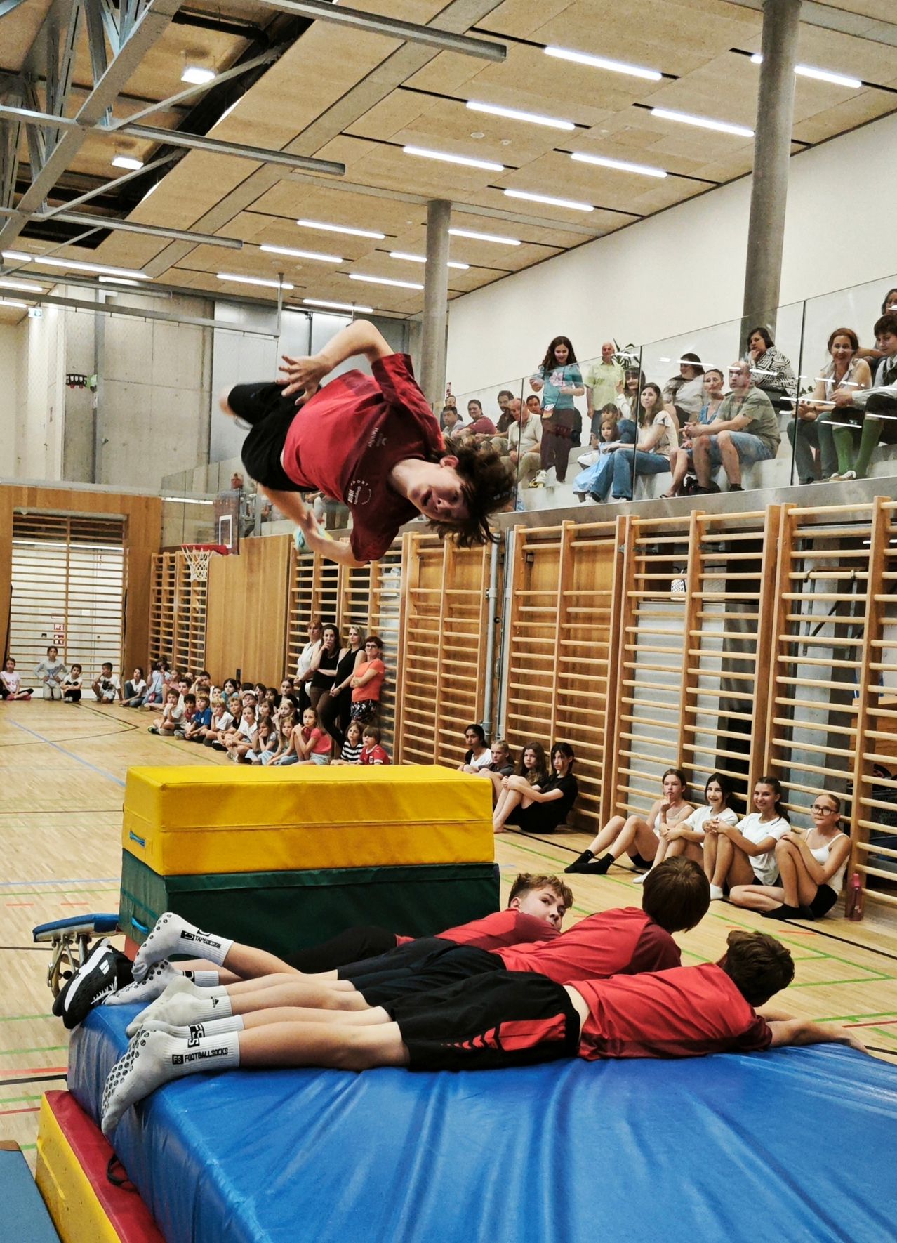 Ein junger Junge führt einen akrobatischen Überschlag über einem Gymnastiktisch durch, während eine Menge von den Tribünen zuschaut.